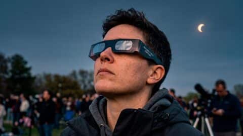 Persona mirando de forma segura un eclipse solar parcial en el cielo utilizando gafas protectoras certificadas ISO 12312-2.