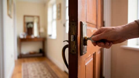 Mano girando una llave en la cerradura de una puerta de madera que se abre hacia el interior de una vivienda alquilada.