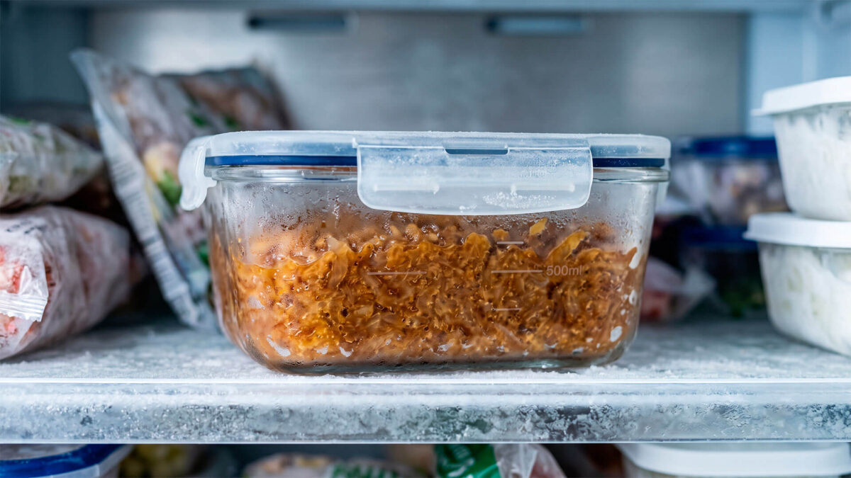 Recipiente de cristal hermético con cebolla caramelizada congelada sobre un estante con escarcha dentro del congelador.