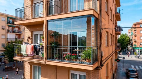 Balcón con cerramiento de cristales en la fachada de un edificio residencial junto a terrazas abiertas.