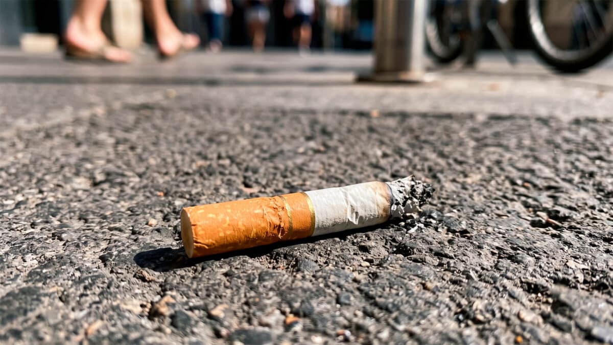 Colilla de cigarro consumida y apagada tirada sobre el suelo de asfalto en una calle urbana.