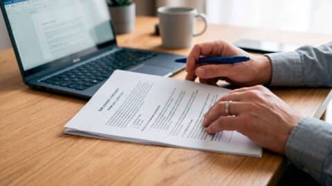 Persona revisando un contrato de trabajo frente a un portátil para trabajar y cobrar el paro.