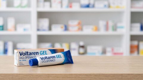 Caja y tubo de Voltaren gel con diclofenaco sobre el mostrador de madera de una farmacia