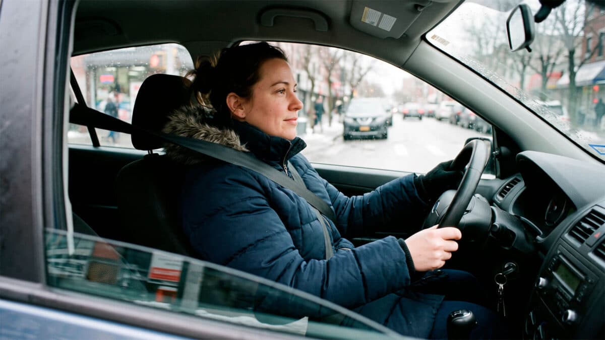 Mujer conduciendo un coche con abrigo de invierno plumas y el cinturón de seguridad abrochado.