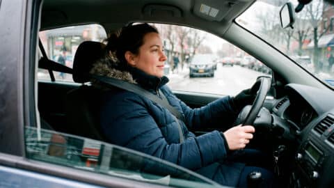 Mujer conduciendo un coche con abrigo de invierno plumas y el cinturón de seguridad abrochado.