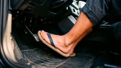 Pies de una persona pisando los pedales del coche mientras conduce con chanclas.