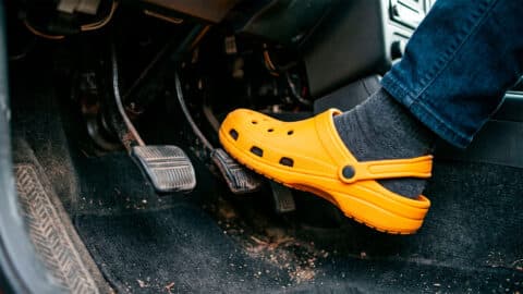 Pie con zueco de goma amarillo pisando el pedal acelerador de un vehículo dentro de la zona de conducción.
