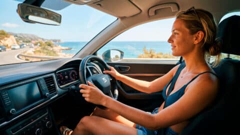 Mujer conduciendo un coche en bikini por una carretera costera durante el verano.
