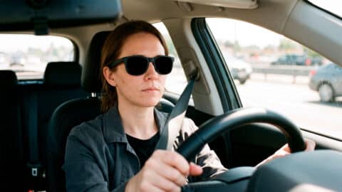 Mujer conduciendo un coche en carretera usando gafas de sol con lentes muy oscuras y opacas.