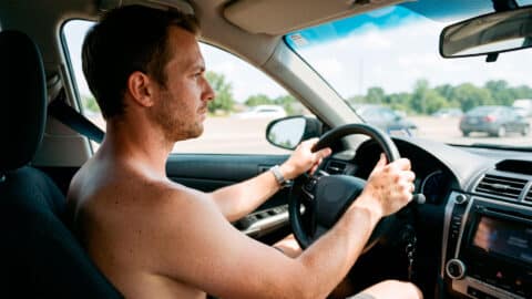 Hombre conduciendo un coche sin camiseta durante un día soleado de verano.