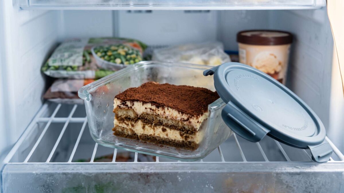 Tiramisú casero con cacao en recipiente hermético de cristal dentro del congelador.
