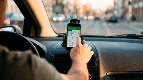 Conductor tocando la pantalla de un móvil con GPS en el soporte del salpicadero.