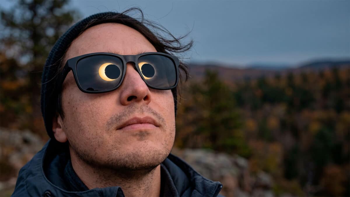 Hombre mirando al cielo con gafas de sol que reflejan un eclipse solar parcial en sus cristales.