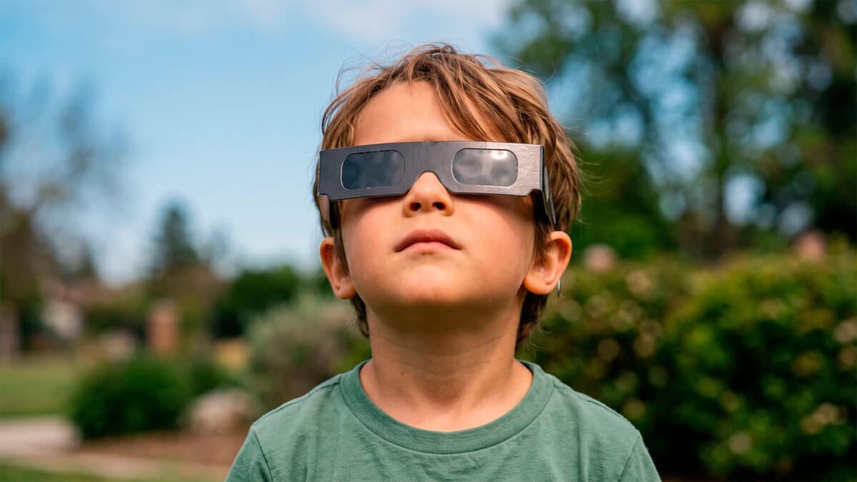 Niño mirando al cielo con gafas especiales de cartón para ver un eclipse solar de forma segura al aire libre.