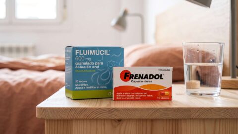 Cajas de Fluimucil y Frenadol junto a un vaso con agua sobre una mesilla de noche de madera.