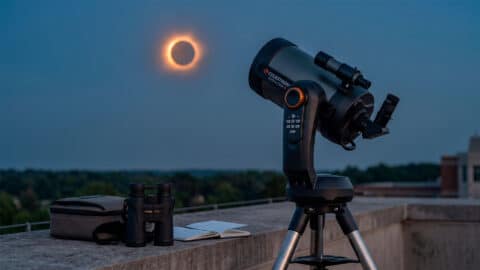 Telescopio Celestron y prismáticos Nikon orientados hacia un eclipse solar total en el cielo al anochecer.