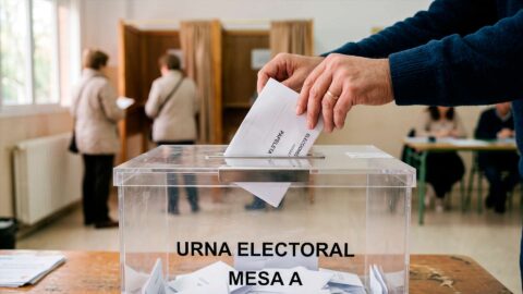 Mano depositando papeleta en urna transparente en colegio electoral de España.